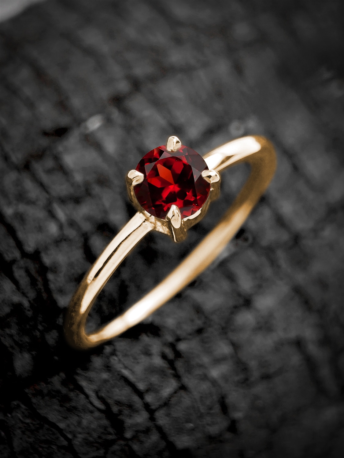 Stylish round garnet engagement ring in yellow gold, showcased on dark stone surface